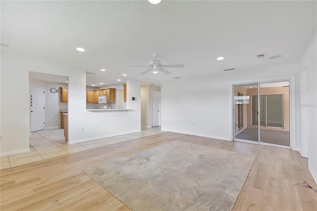 A living room with light wood flooring, a ceiling fan, and an open kitchen view — 1980 SUMMER COURT, KISSIMMEE, FL