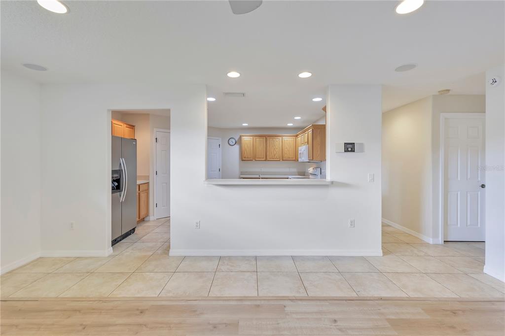A kitchen with light wood cabinets and a pass-through window overlooks a tiled floor area — 1980 SUMMER COURT, KISSIMMEE, FL