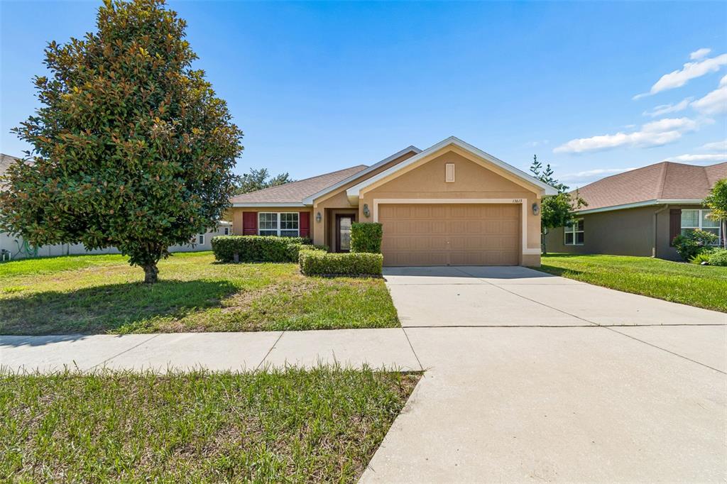 A single-story suburban house with a tan stucco exterior, a two-car garage, and a large tree — 13613 NITI DRIVE, HUDSON, FL