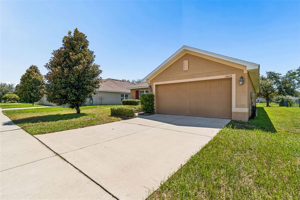 A tan single-story house features a two-car garage, a concrete driveway, and a grassy lawn — 13613 NITI DRIVE, HUDSON, FL