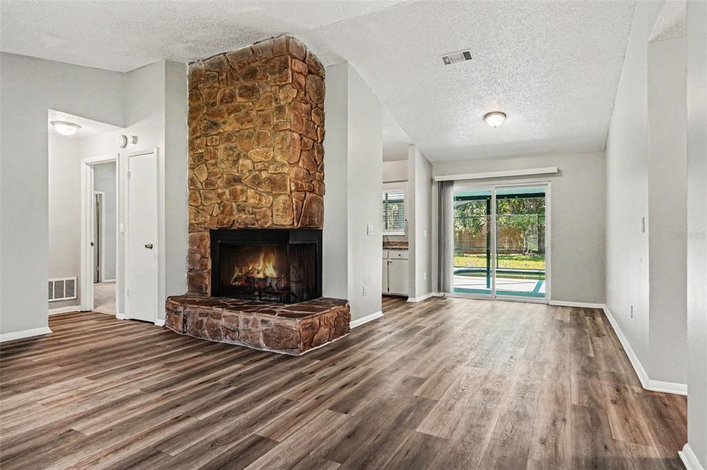A living room features wood-look flooring, a stone corner fireplace, and sliding glass patio doors — 629 ALTON ROAD, WINTER SPRINGS, FL