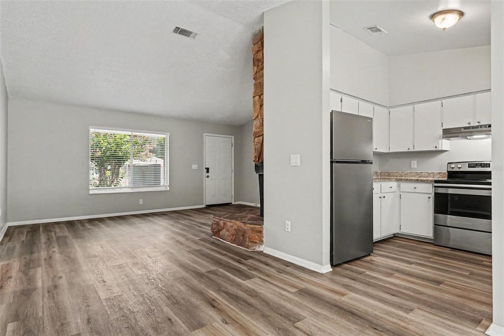 A living room with wood-look flooring and a stone fireplace connects to a white kitchen — 629 ALTON ROAD, WINTER SPRINGS, FL