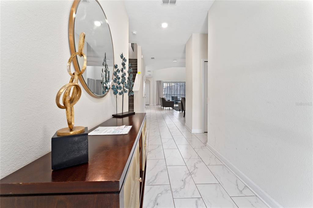 A hallway with white marble-look tile flooring leads toward a living area with furniture — 2734 BOOKMARK DRIVE, KISSIMMEE, FL