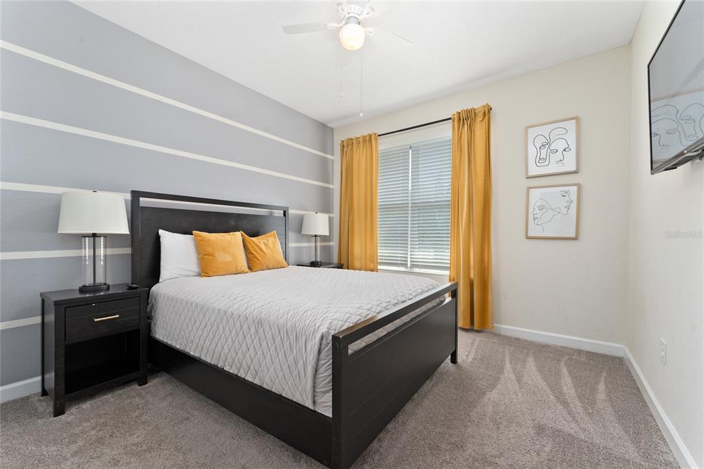 A bedroom features a dark wood bed frame, striped gray wall, and yellow curtains — 2734 BOOKMARK DRIVE, KISSIMMEE, FL