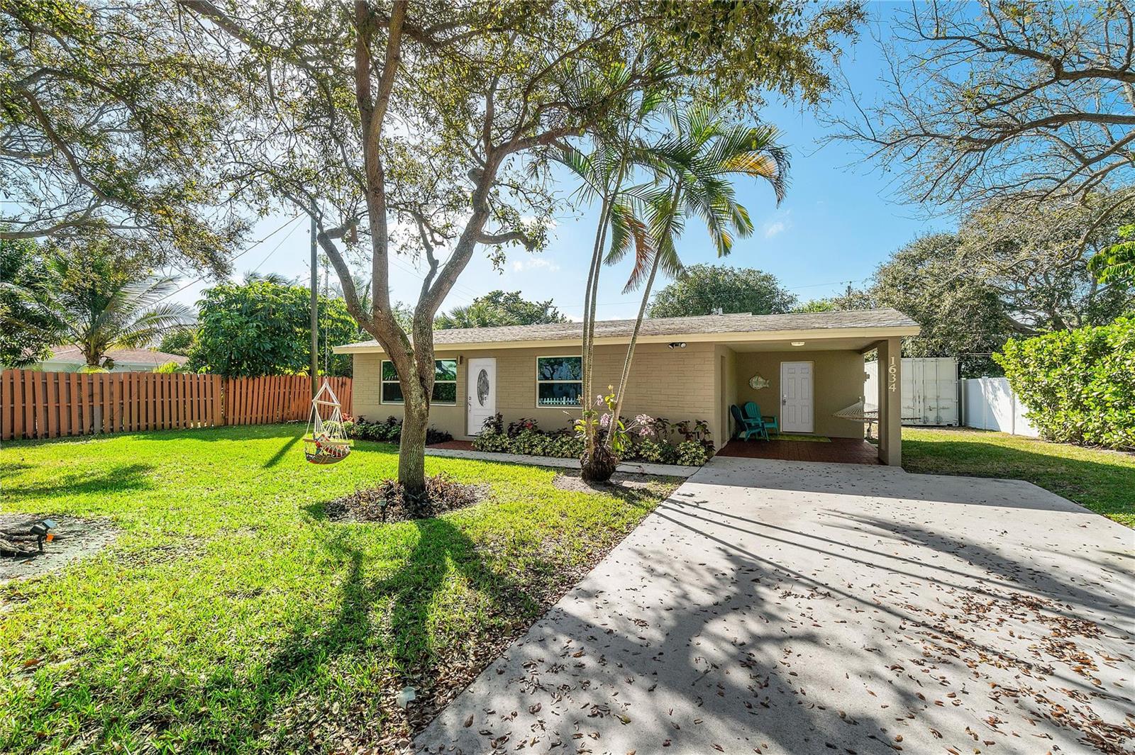 A single-story tan house with a concrete driveway, a front porch, and a large tree — 1634 NE 3rd Avenue, Delray Beach FL 33444, DELRAY BEACH, FL