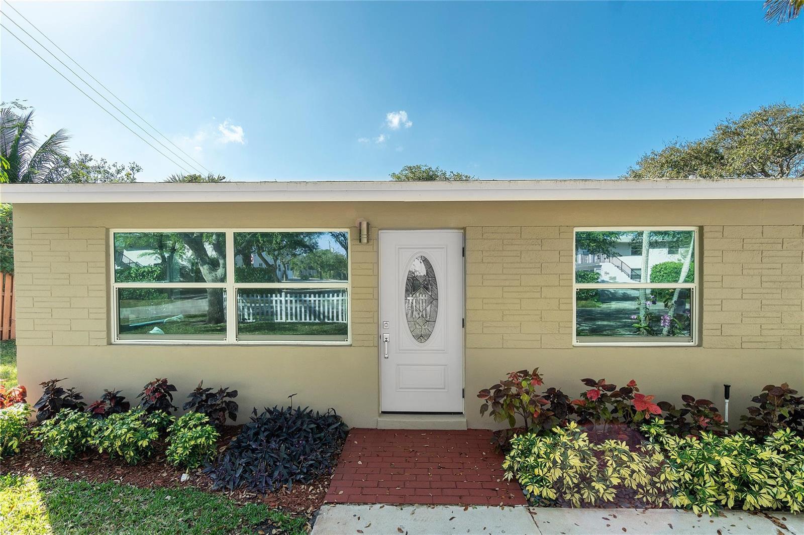 The exterior of a beige, single-story house features a white front door and two windows — 1634 NE 3rd Avenue, Delray Beach FL 33444, DELRAY BEACH, FL