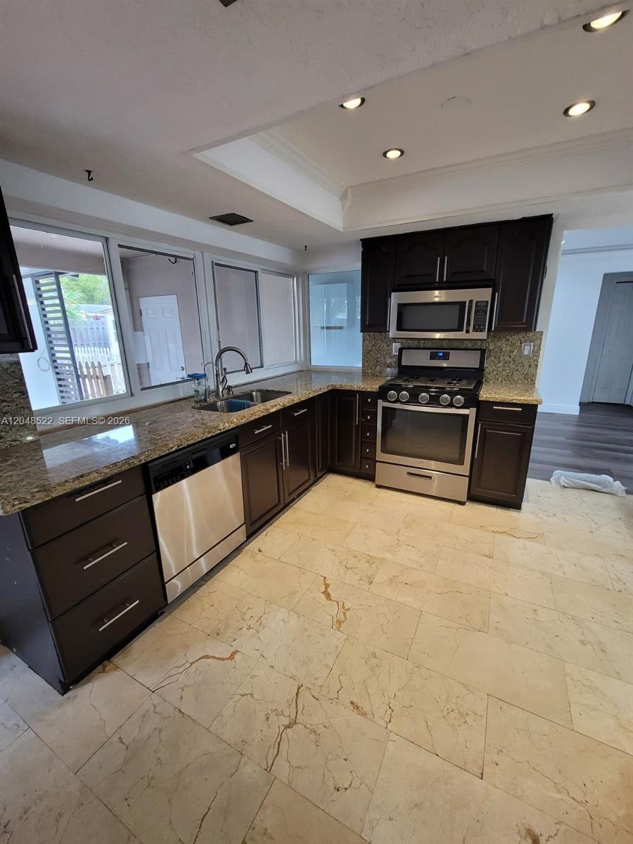 A kitchen features dark wood cabinets, granite countertops, stainless steel appliances, and light tile flooring — 8461 NW 27th Pl, Sunrise FL 33322, SUNRISE, FL