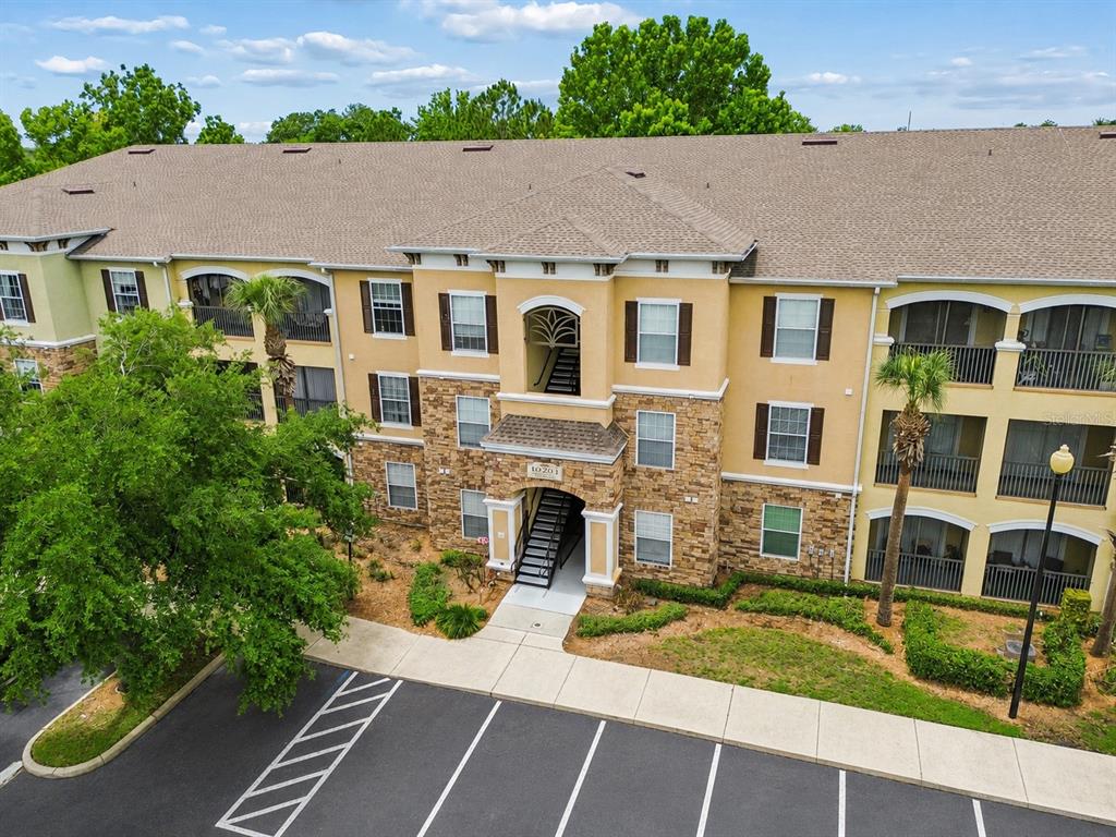 An exterior view of a three-story apartment building with tan stucco and stone veneer siding — 10203 COURTNEY PALMS BOULEVARD UNIT 103, TAMPA, FL