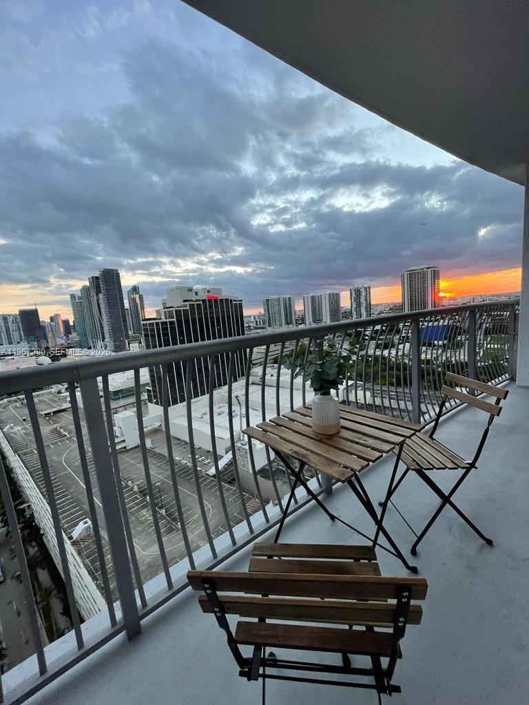 A balcony features a small wooden table and two chairs overlooking a city skyline at sunset — 1750 N Bayshore Dr # 2710, Miami FL 33132, MIAMI, FL