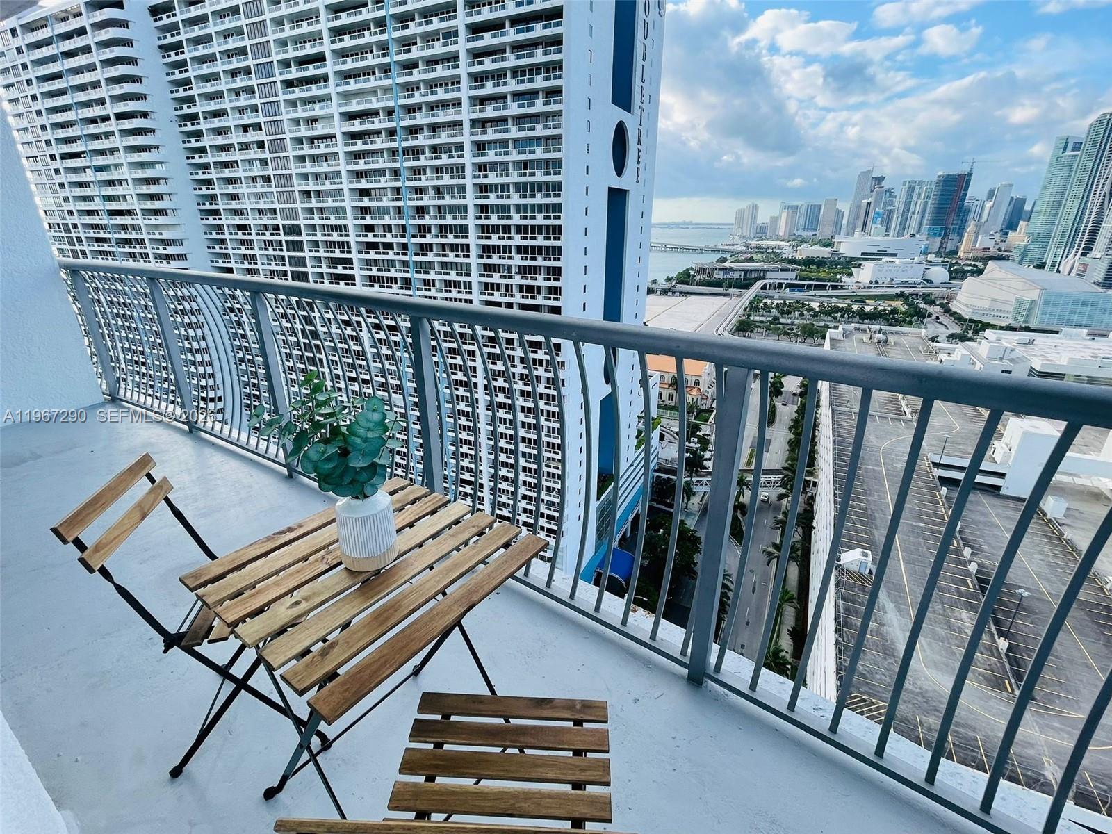 A balcony features a small wooden table and chairs overlooking a city skyline and bay — 1750 N Bayshore Dr # 2710, Miami FL 33132, MIAMI, FL