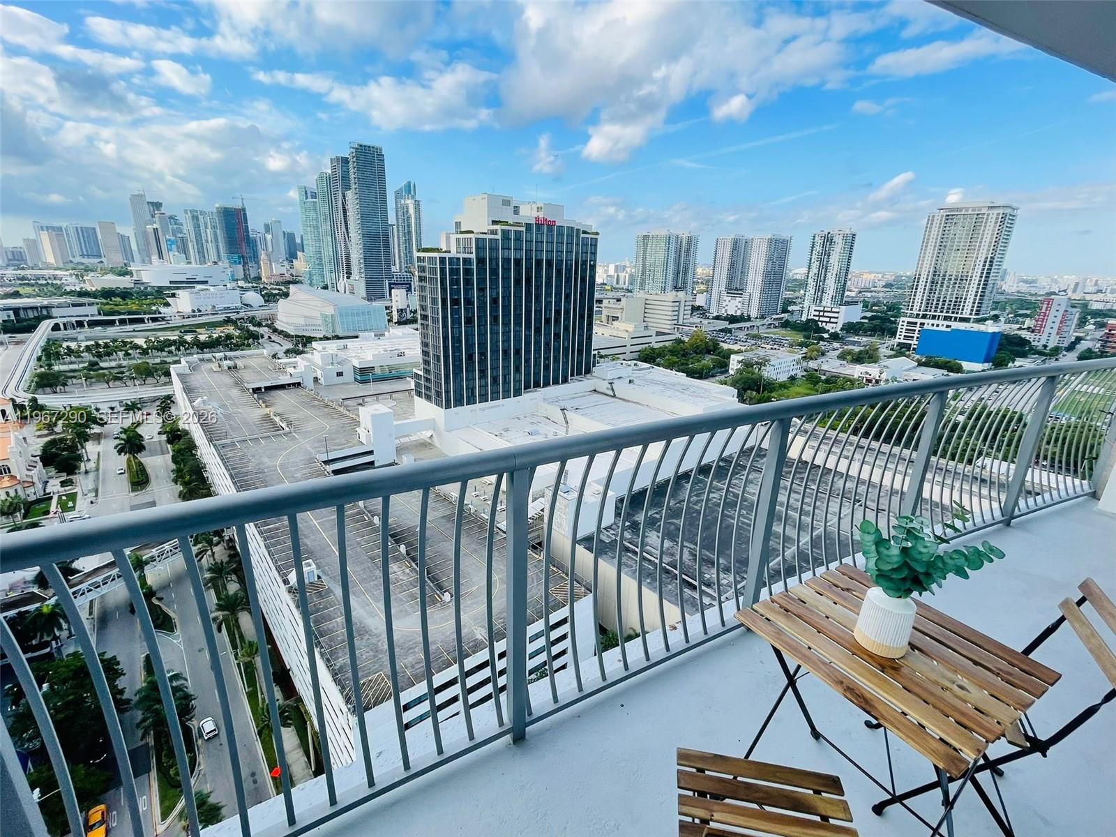 A high-rise balcony overlooks a city skyline with a small wooden table and chairs — 1750 N Bayshore Dr # 2710, Miami FL 33132, MIAMI, FL