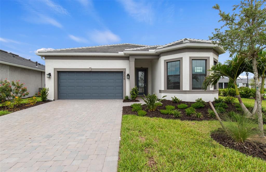 A single-story house features a gray garage, white stucco walls, and a paved driveway — 5006 GOLDEN SHORE COURT, LAKEWOOD RANCH, FL