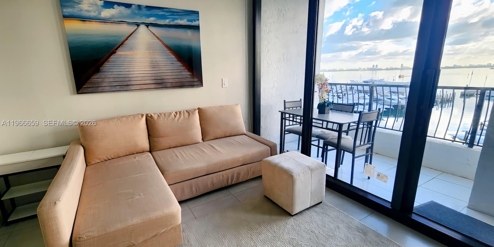A living room features a beige sectional sofa, a matching ottoman, and a balcony view — 555 NE 15th St # 516, Miami FL 33132, MIAMI, FL