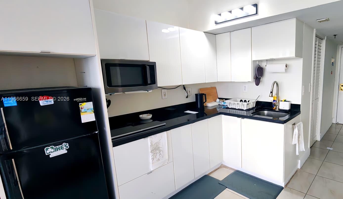 A small kitchen features white cabinets, black countertops, a black refrigerator, and a microwave — 555 NE 15th St # 516, Miami FL 33132, MIAMI, FL