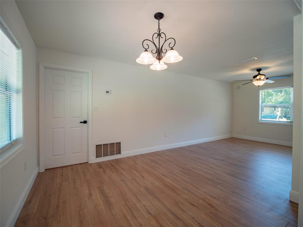 An empty room features light wood-look flooring, white walls, a chandelier, and a ceiling fan — 1408 6TH STREET NW, LIVE OAK, FL