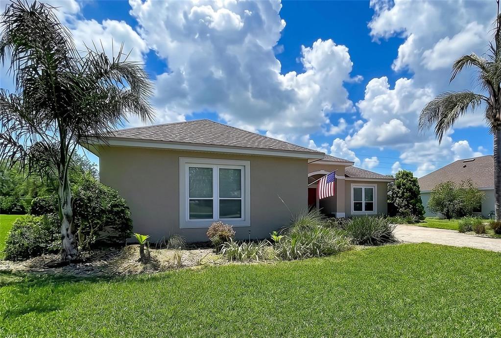 A single-story house with a paved driveway, tan exterior, and a front-facing American flag — 408 TALAMONE DRIVE, WINTER HAVEN, FL