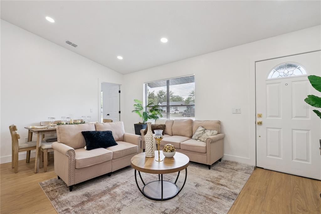A living room features two beige sofas, a round coffee table, and a dining area — 65 S COURTLAND BOULEVARD, DELTONA, FL