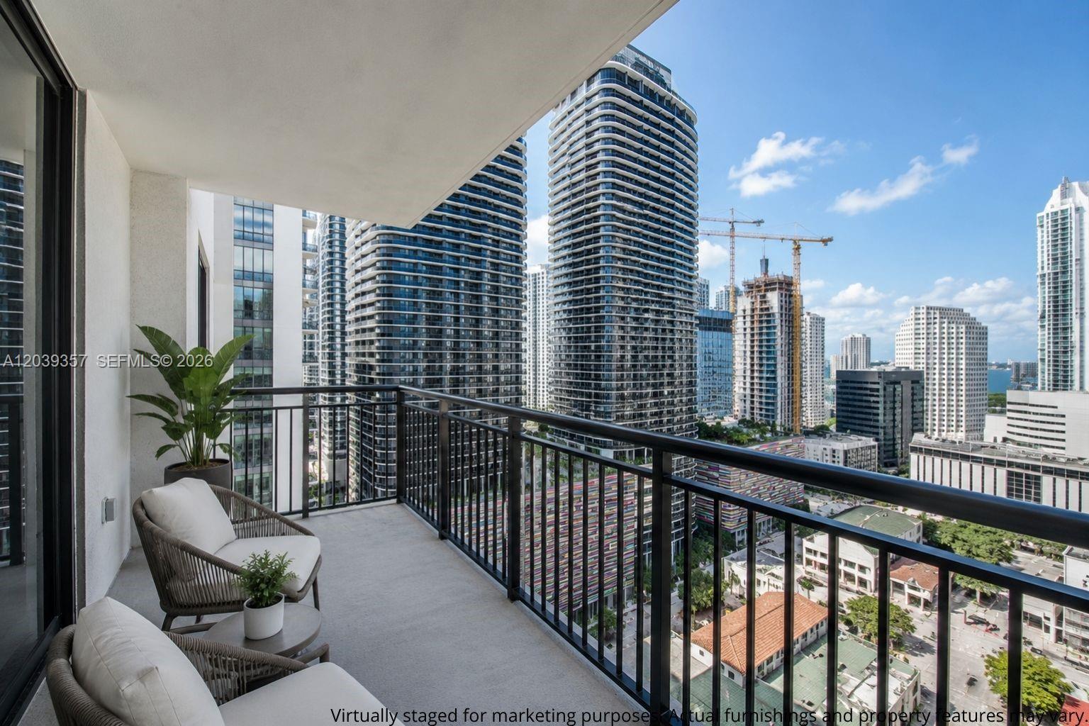 A balcony with two chairs and a small table overlooks a dense urban skyline — 999 SW 1st Ave # 2402, Miami FL 33130, MIAMI, FL