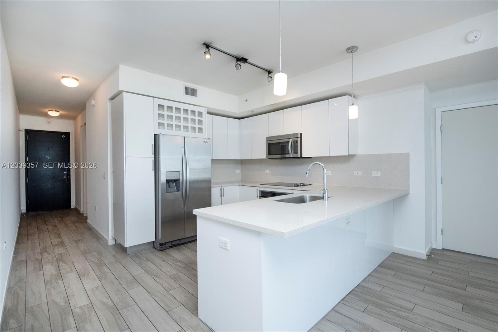 A modern kitchen features white cabinetry, stainless steel appliances, and a quartz-topped island — 999 SW 1st Ave # 2402, Miami FL 33130, MIAMI, FL
