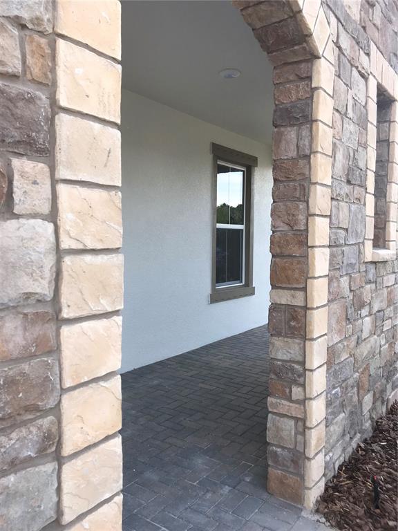 A stone-arched entryway leads to a covered porch with a window and paver flooring — 11638 SWEET TANGERINE LANE, TAMPA, FL