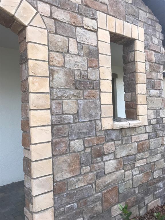 A stone-clad exterior wall features a rectangular window and an arched entryway with light-colored quoins — 11638 SWEET TANGERINE LANE, TAMPA, FL