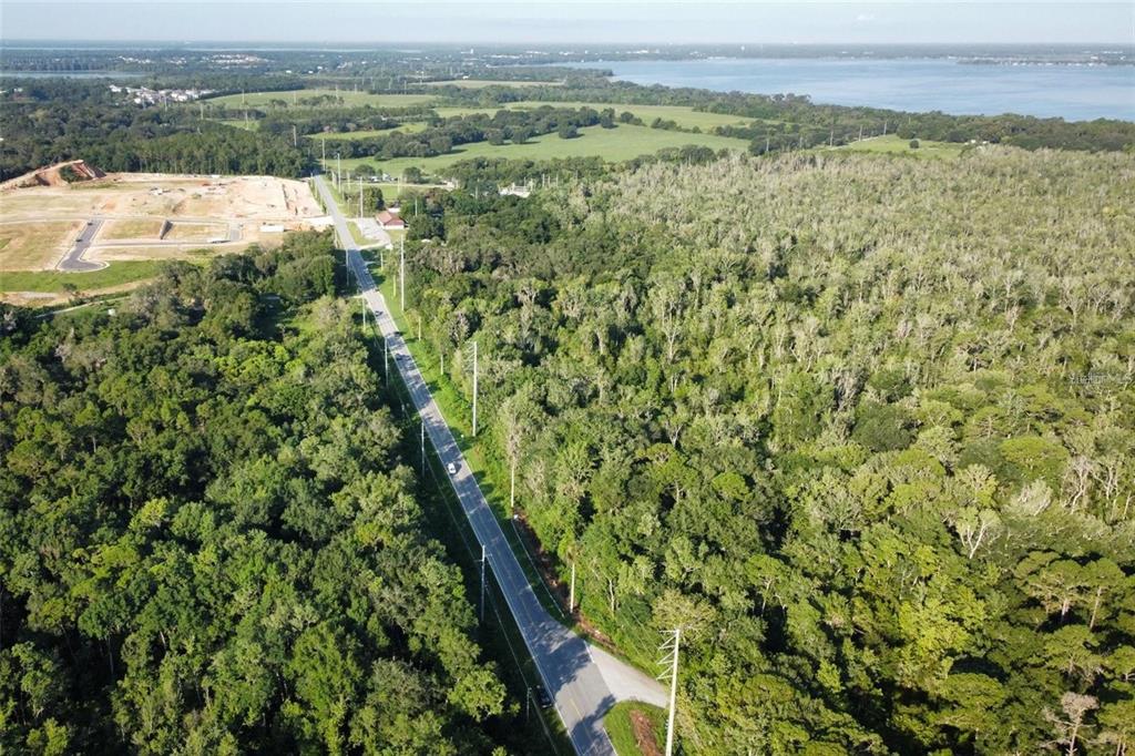 An aerial view shows a road running through a dense forest toward a distant lake — 8915 COUNTY ROAD 44, LEESBURG, FL