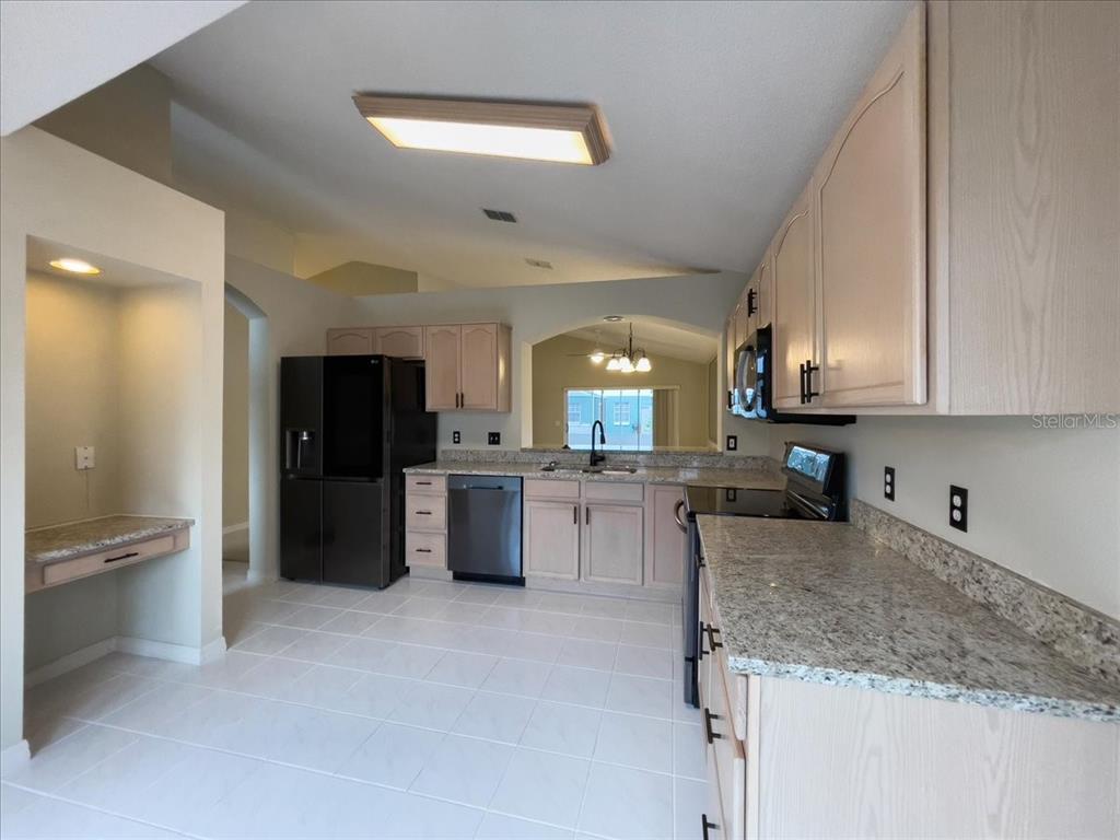 A kitchen features light wood cabinets, granite countertops, black appliances, and white tile flooring — 218 LANGFORD PARK DRIVE, DAVENPORT, FL