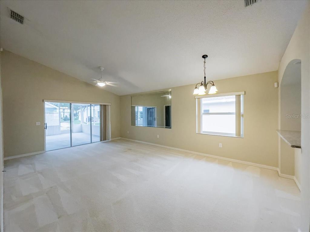 A living room features beige carpet, a vaulted ceiling, a sliding glass door, and mirrors — 218 LANGFORD PARK DRIVE, DAVENPORT, FL
