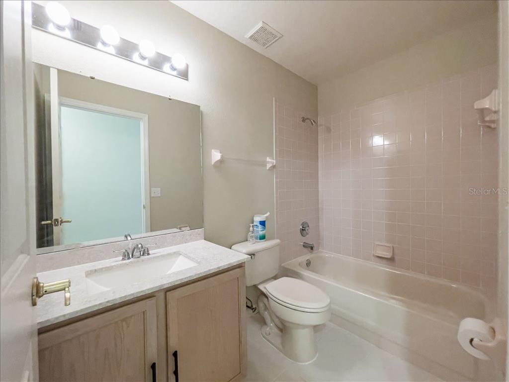 A bathroom features a vanity with a stone countertop, a toilet, and a tiled shower-tub — 218 LANGFORD PARK DRIVE, DAVENPORT, FL