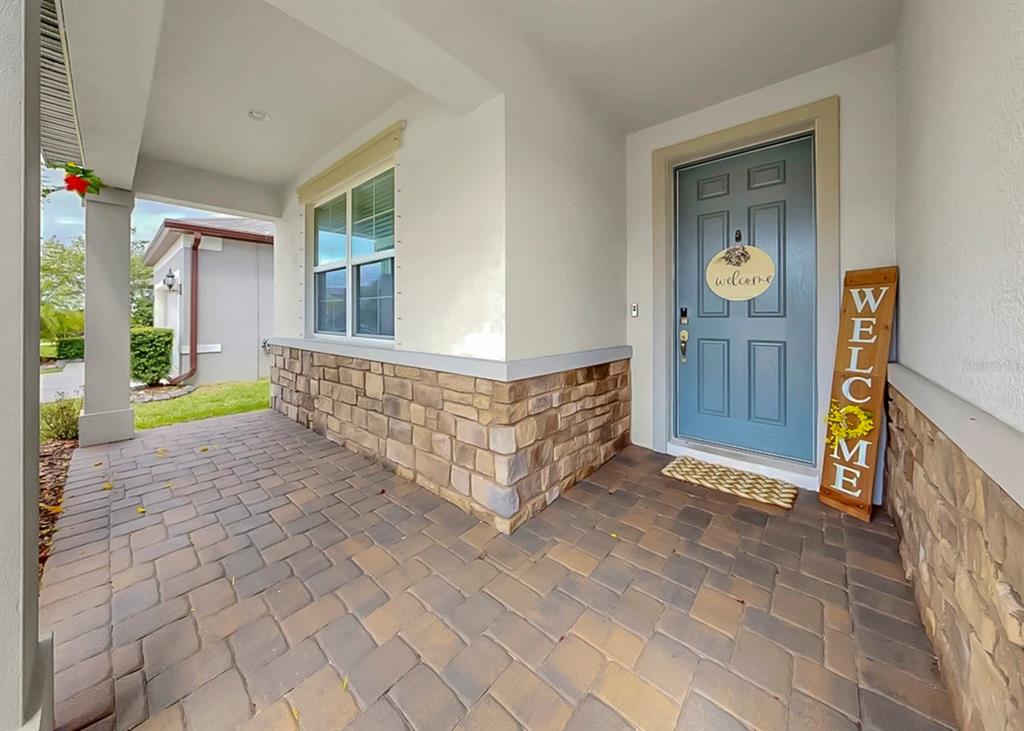 A covered front porch with stone veneer siding, a blue door, and paver flooring — 10322 WINE PRESS AVENUE, RIVERVIEW, FL