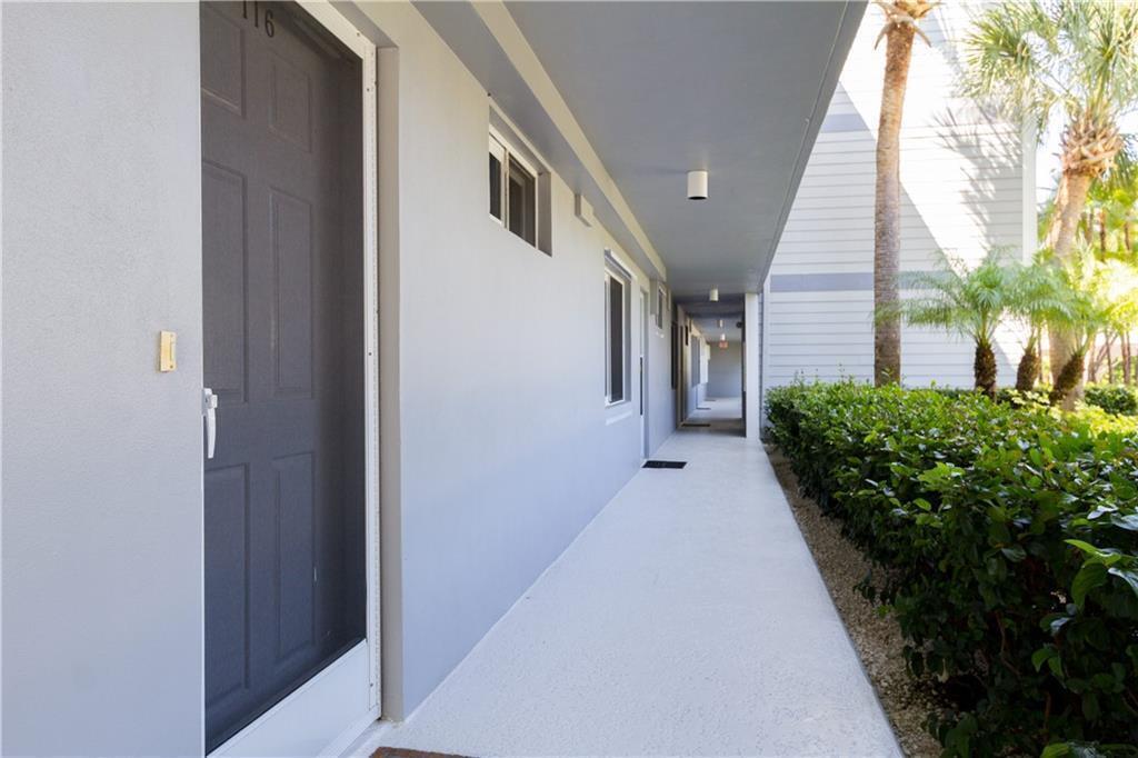 An outdoor walkway leads past a gray door and windows along the side of a building — VERO BEACH, FL