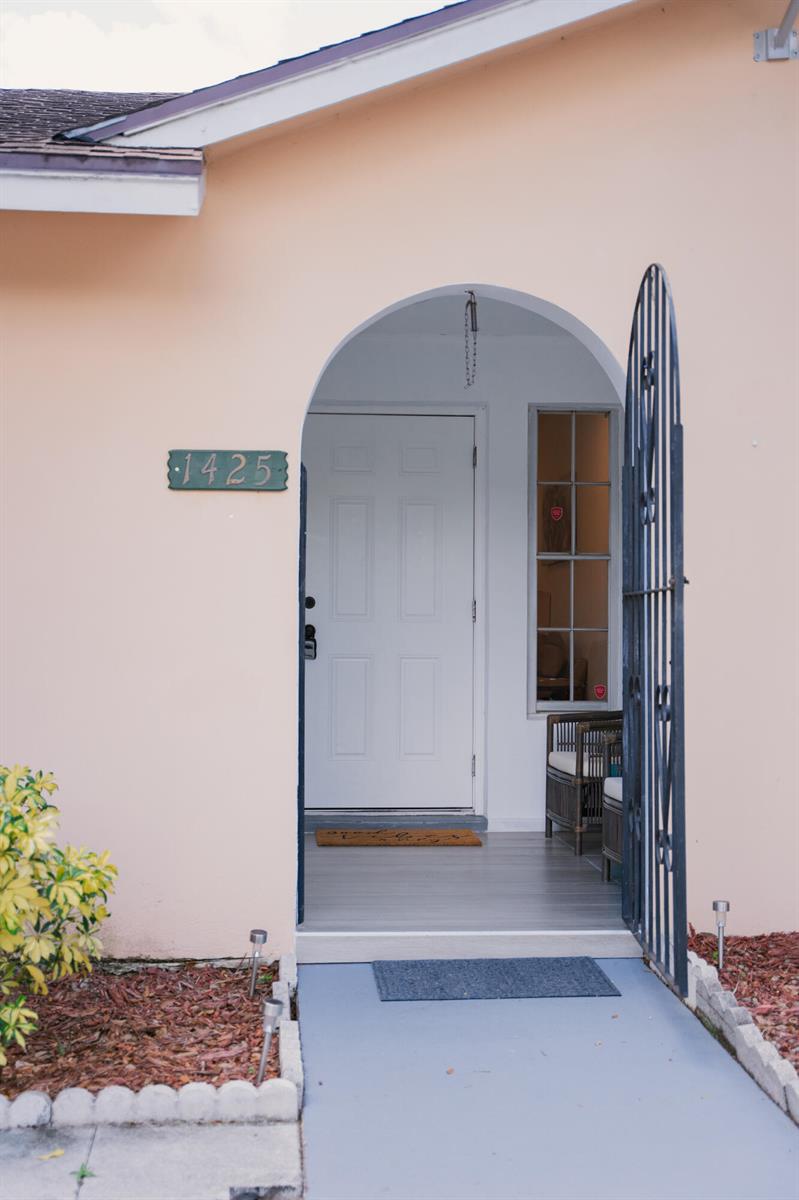 The exterior of a peach-colored home features an arched entryway with a white front door — 1425 Riverside Circle, Wellington FL 33414, WELLINGTON, FL