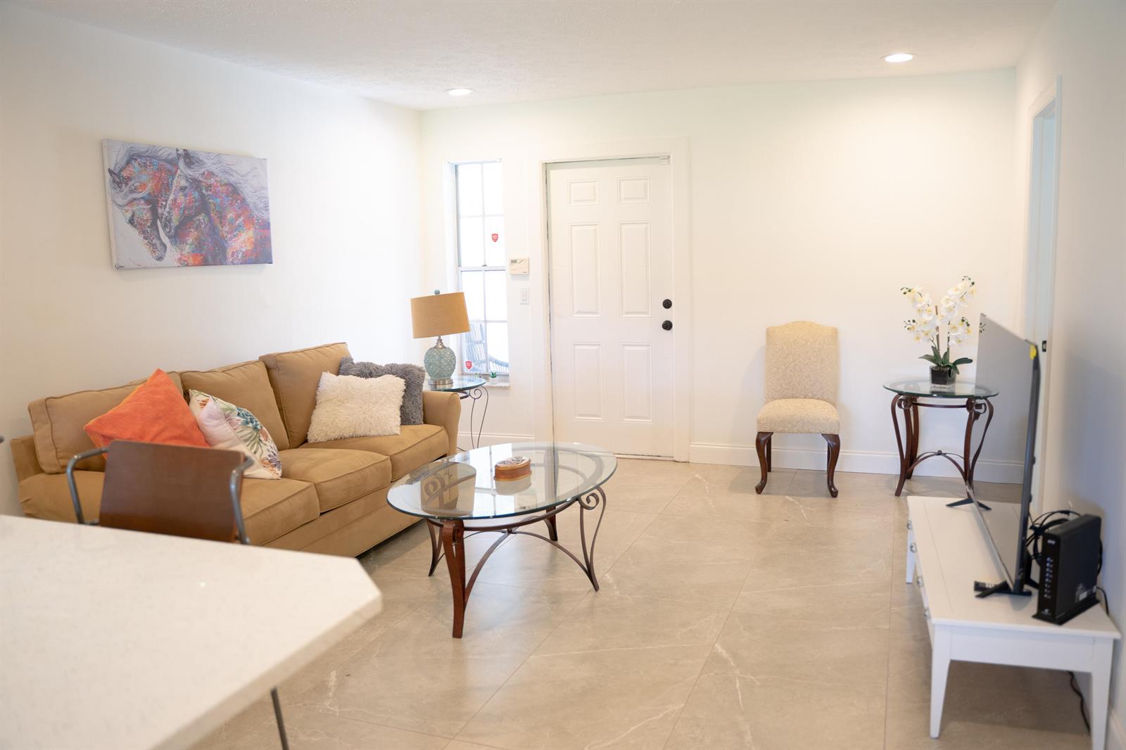 A living room features a tan sofa, glass coffee table, tile flooring, and a white door — 1425 Riverside Circle, Wellington FL 33414, WELLINGTON, FL