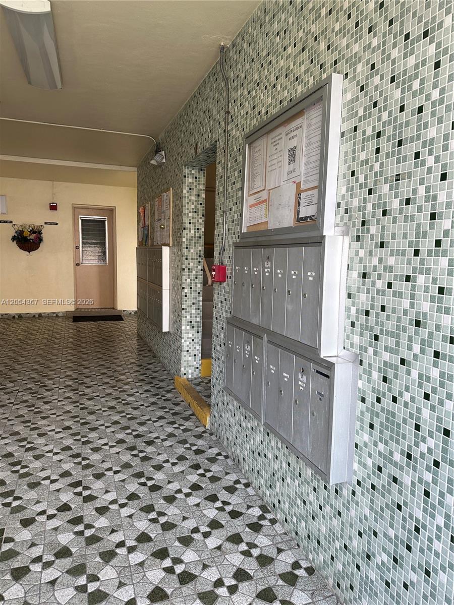 An indoor apartment building hallway features tiled walls, patterned flooring, and a bank of mailboxes — 17050 NE 14th Ave # 110, Miami FL 33162, MIAMI, FL