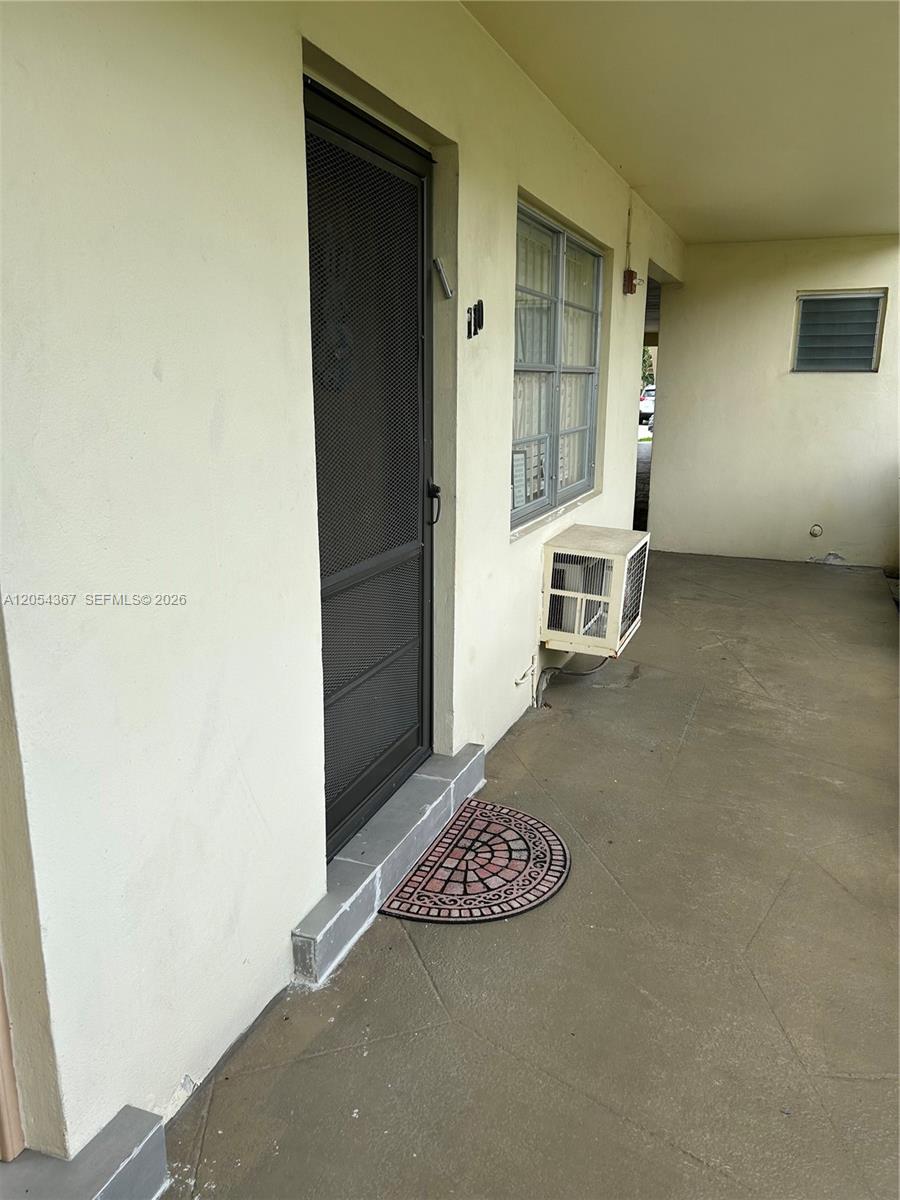 A concrete walkway leads to a front door with a screen and a window unit — 17050 NE 14th Ave # 110, Miami FL 33162, MIAMI, FL