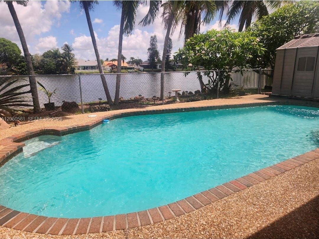 A backyard swimming pool with a brick border overlooks a lake behind a chain-link fence — 11711 NW 35th St, Sunrise FL 33323, SUNRISE, FL