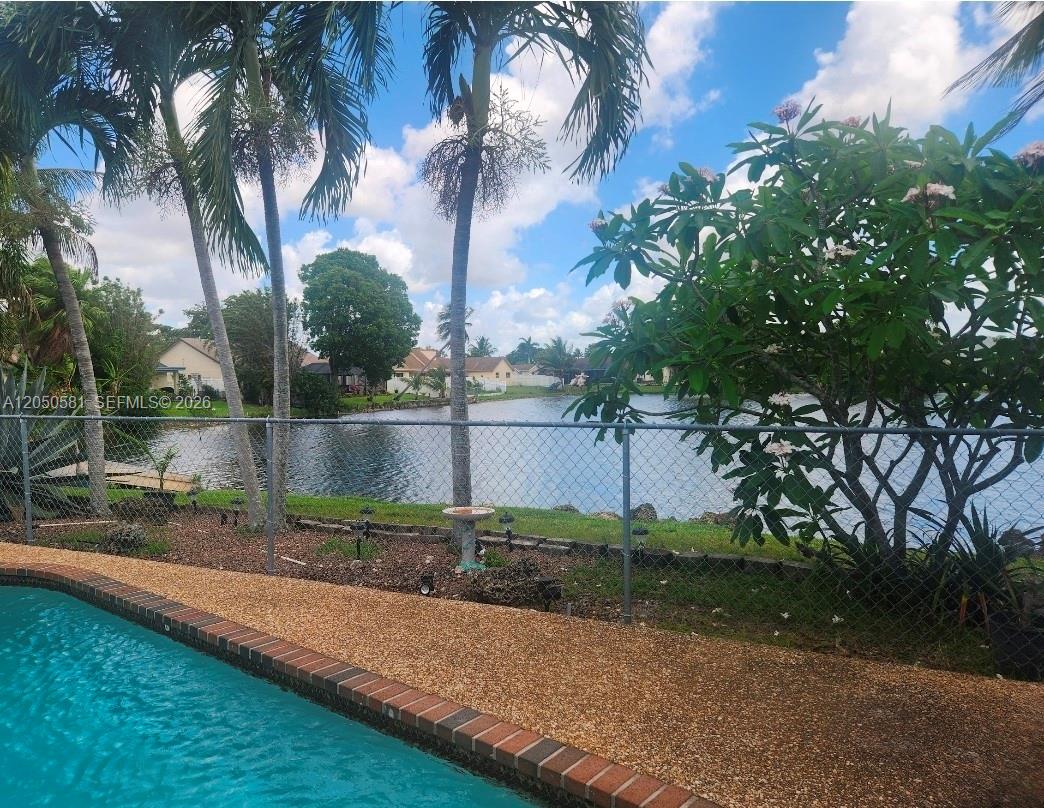 A swimming pool overlooks a lake behind a chain-link fence and palm trees — 11711 NW 35th St, Sunrise FL 33323, SUNRISE, FL
