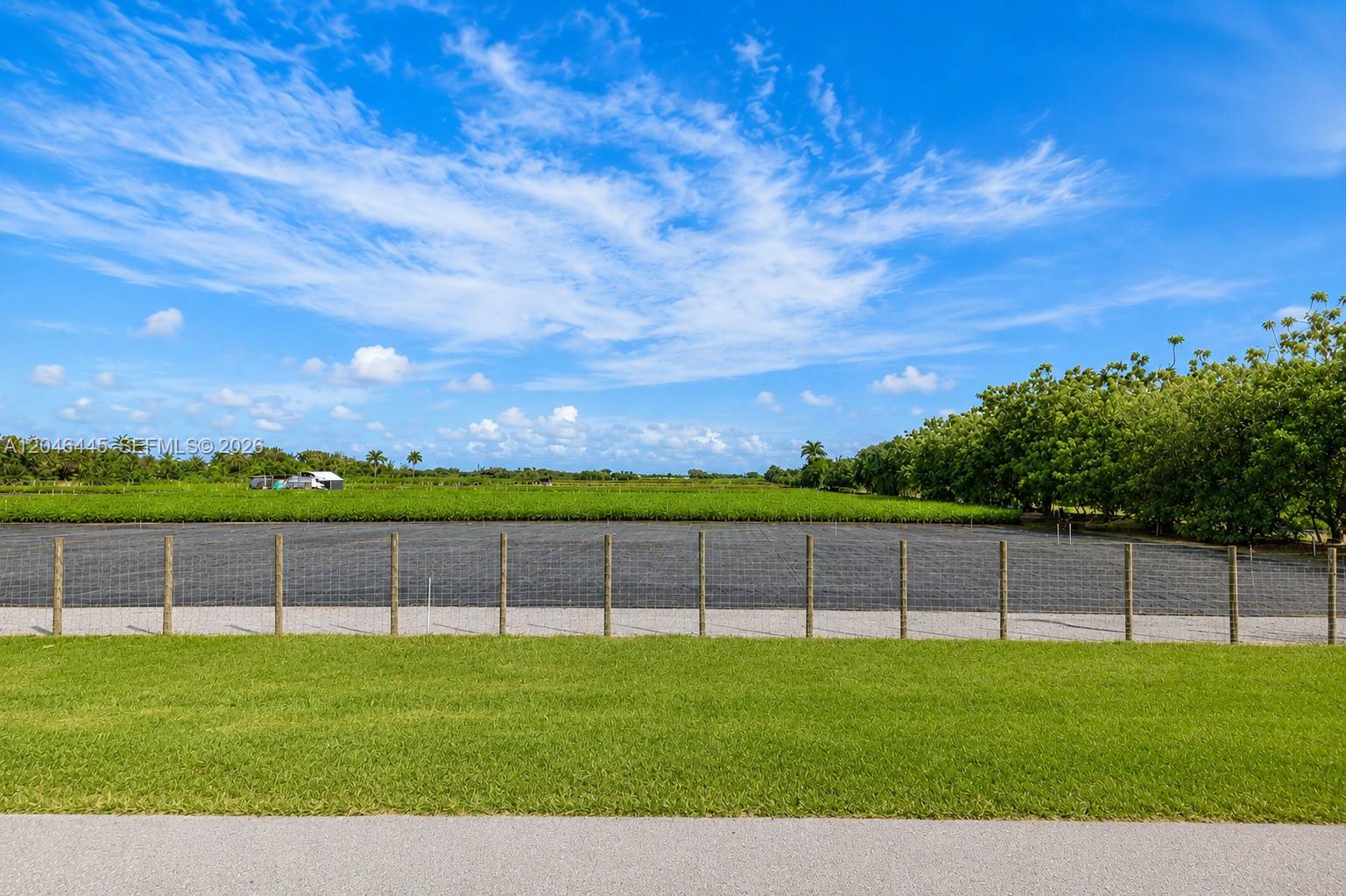 A wire fence separates a grassy foreground from a large field covered in black fabric — 17345 SW 216th St, Miami FL 33170, MIAMI, FL