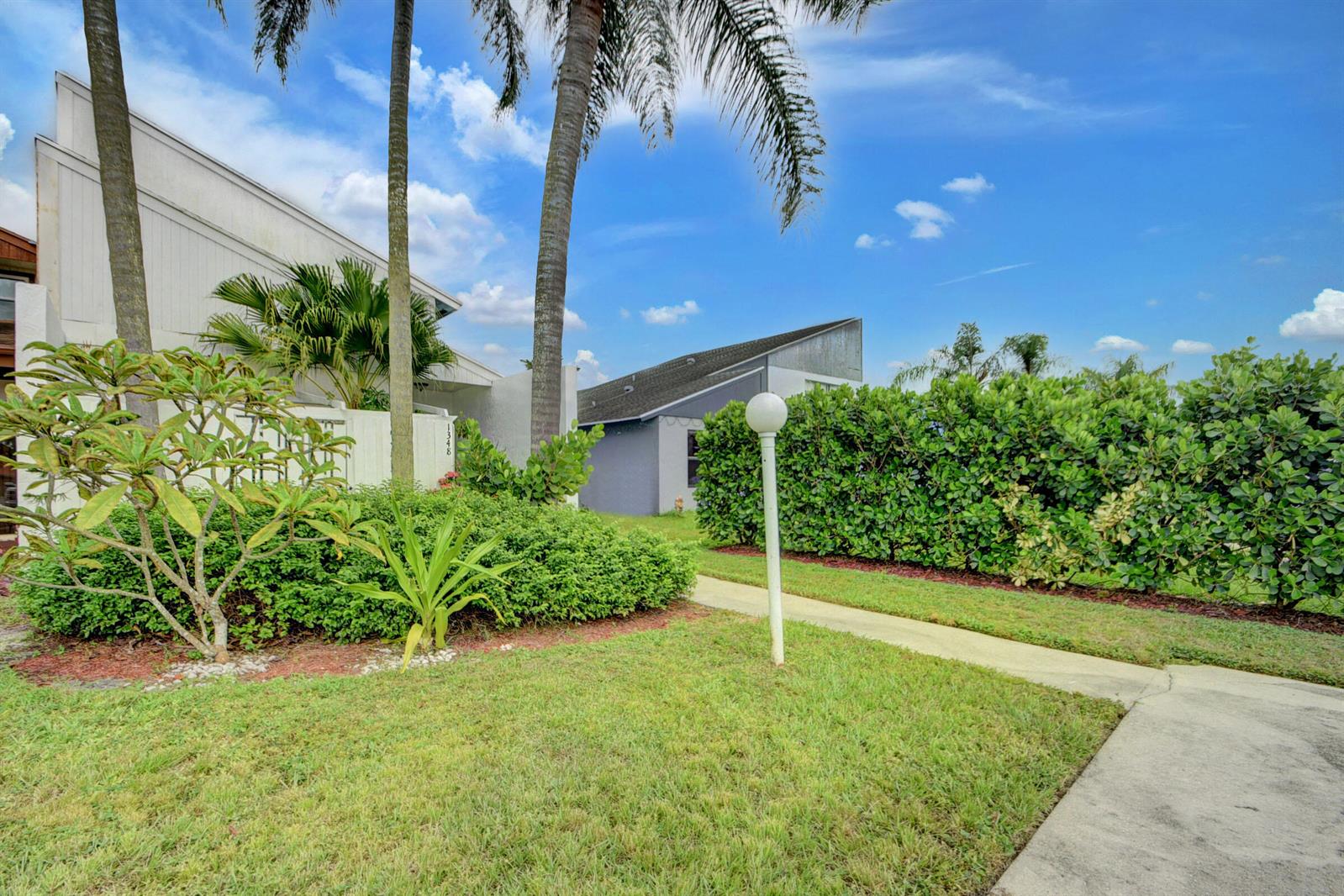 A grassy yard with palm trees, a walkway, and a hedge next to a building — 1348 The 12th Fairway, Wellington FL 33414, WELLINGTON, FL