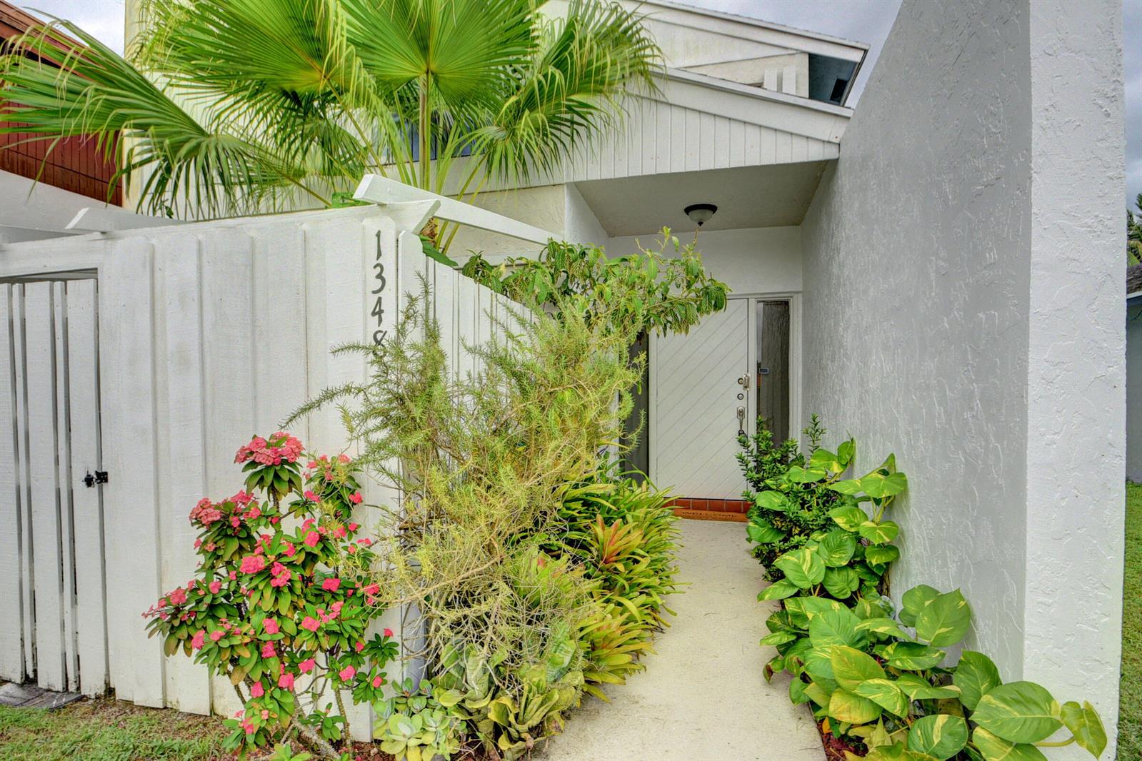 A white house exterior features a gated walkway leading to a front door with landscaping — 1348 The 12th Fairway, Wellington FL 33414, WELLINGTON, FL