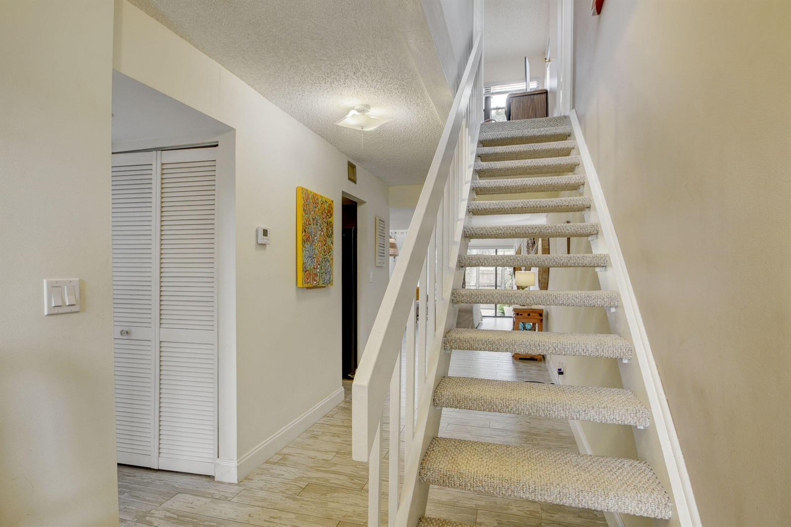 A carpeted staircase with white railings leads to an upper level in a bright hallway — 1348 The 12th Fairway, Wellington FL 33414, WELLINGTON, FL