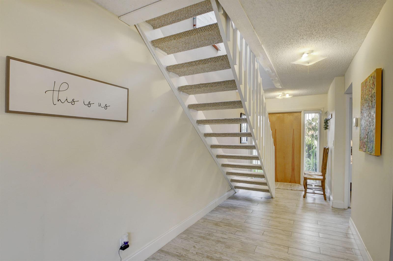An entryway features a white staircase with carpeted treads, light wood-look flooring, and wall art — 1348 The 12th Fairway, Wellington FL 33414, WELLINGTON, FL