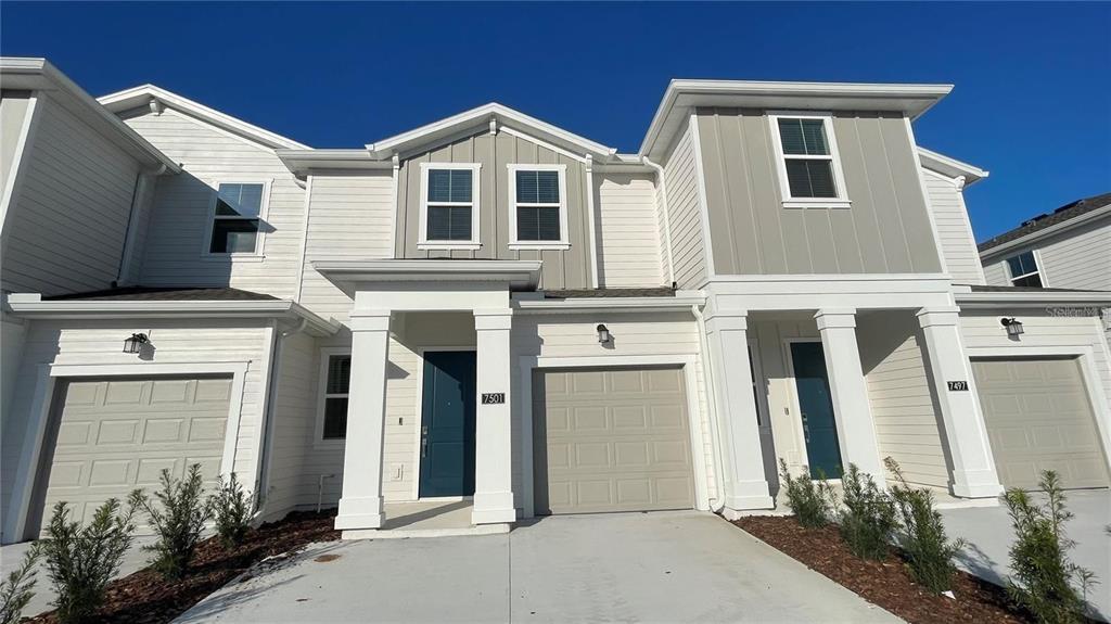 A row of three modern townhouses with white siding, gray accents, and attached garages — 7501 STONE CREEK TRAIL, KISSIMMEE, FL
