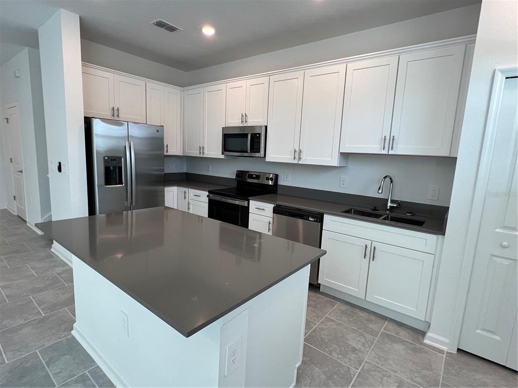 A kitchen features white cabinetry, stainless steel appliances, and a gray island with quartz countertops — 7501 STONE CREEK TRAIL, KISSIMMEE, FL