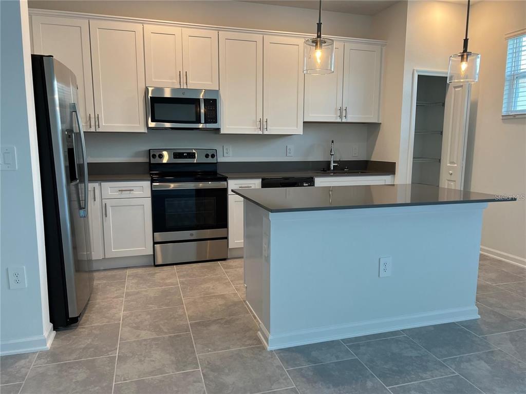 A kitchen features white cabinets, stainless steel appliances, a gray island, and tile flooring — 7501 STONE CREEK TRAIL, KISSIMMEE, FL
