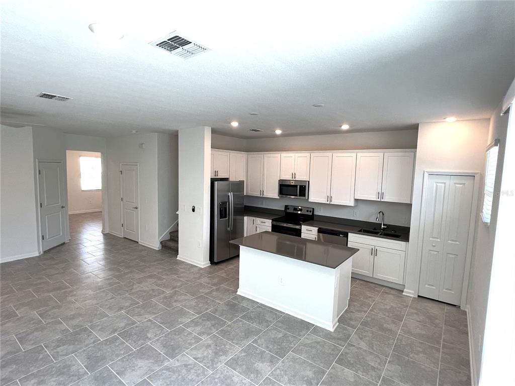 A kitchen with white cabinets, dark countertops, a center island, and gray tile flooring — 7501 STONE CREEK TRAIL, KISSIMMEE, FL