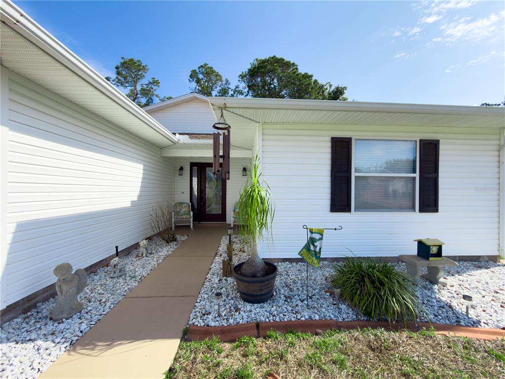 The exterior of a white-sided house features a concrete walkway leading to the front entrance — 32676 OAK PARK DRIVE, LEESBURG, FL