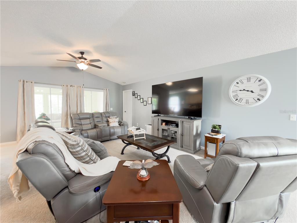 A living room features gray leather furniture, a large television, and a wall clock — 32676 OAK PARK DRIVE, LEESBURG, FL