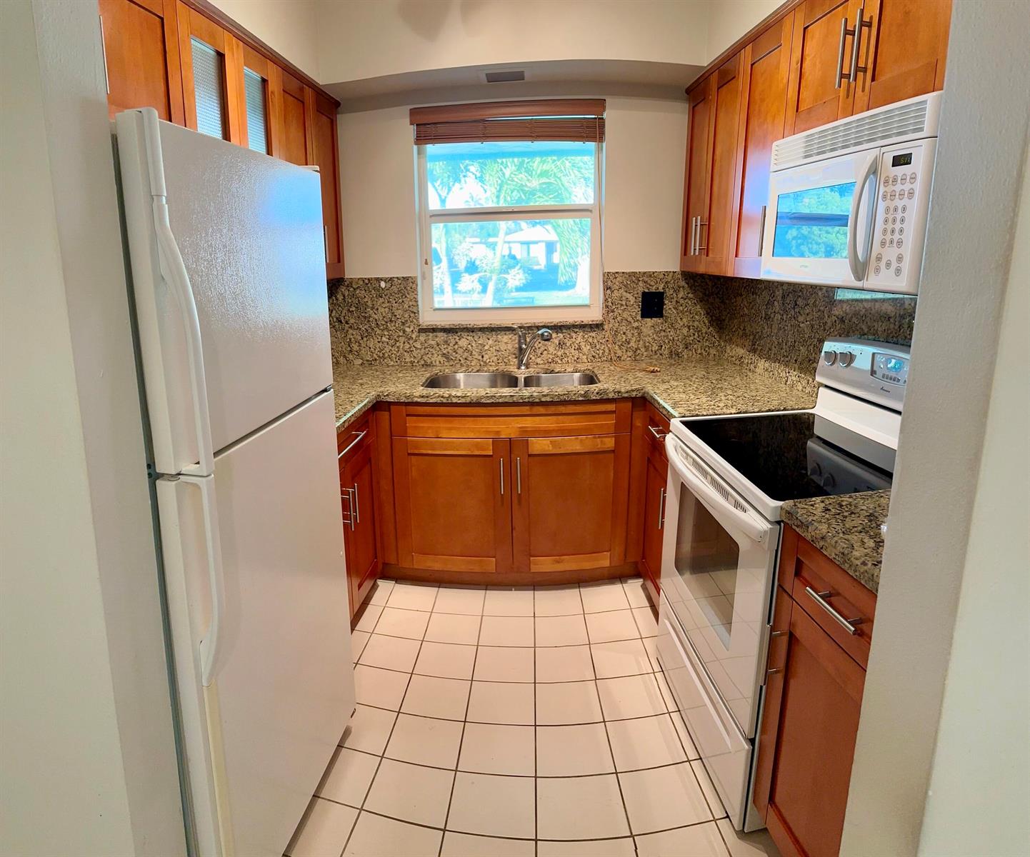 A galley kitchen features wood cabinets, granite countertops, white appliances, and a tiled floor — 3801 NE 22nd Terrace # 11, Lighthouse Point FL 33064, LIGHTHOUSE POINT, FL