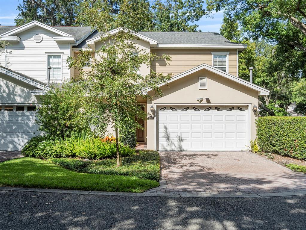 A two-story townhouse with a beige stucco facade, white garage door, and paved driveway — 1223 COUNTRY CLUB OAKS CIRCLE, ORLANDO, FL